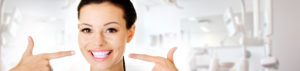 a woman with a full set of veneers smiling and pointing to them