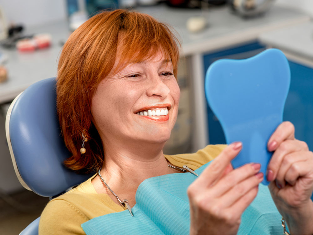 a lady with a full arch of implants smiling into a mirror