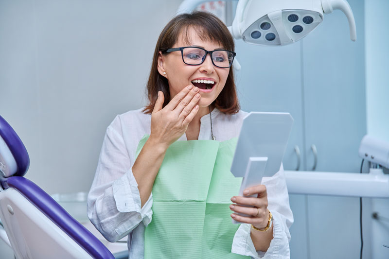 Middle-aged female in dental office looking in mirror