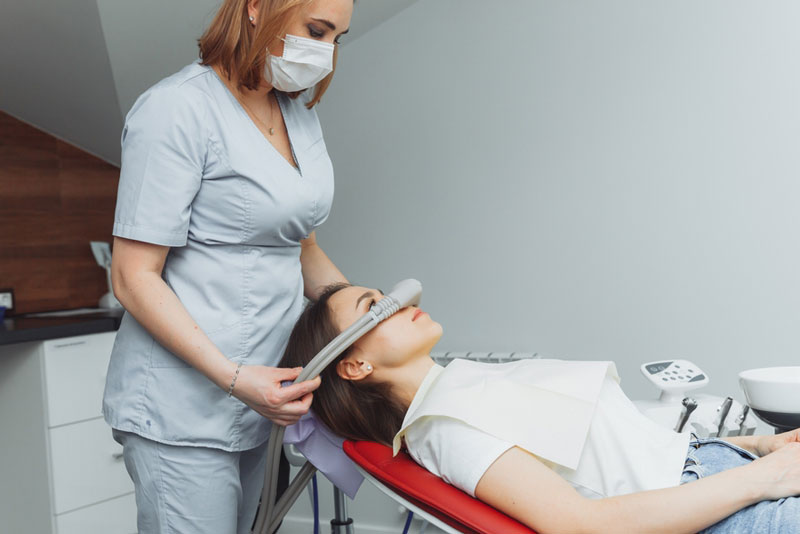 Dental professional administering nitrous oxide sedation to a female patient reclining in a dental chair during treatment.